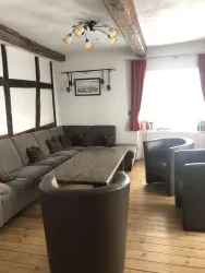 Ein gemütlicher Wohnraum mit einem großen, einladenden Sofa und einem Holztisch. Helle Wände und große Fenster sorgen für eine angenehme Atmosphäre.