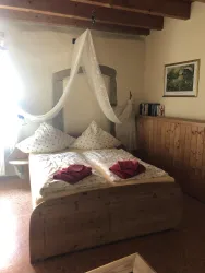 Ein gemütliches Schlafzimmer mit einem Holzbett und dekorativen Kissen. Ein zarter Vorhang hängt über dem Bett und bringt eine entspannte Atmosphäre.