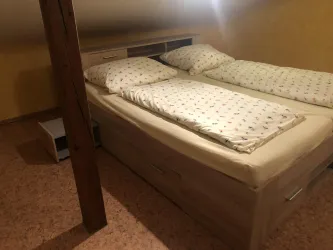 Ein einfaches Schlafzimmer mit zwei Betten und Bettwäsche. Die Wände sind gelb und der Boden ist aus Holz.