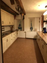 Eine helle Küche mit weißen Schränken und Holzregalen. Zwei Fenster sorgen für natürliches Licht und eine einladende Atmosphäre.