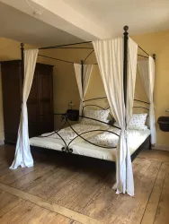 Ein gemütliches Schlafzimmer mit einem Himmelbett und weißen Vorhängen. Der Boden ist aus Holz und die Wände sind in warmen Gelbtönen gestrichen.
