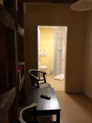 Ein gemütlicher Raum mit einem kleinen Tisch und zwei Stühlen. Im Hintergrund ist ein Badezimmer mit Dusche und WC sichtbar.