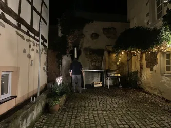 Ein gemauerter Innenhof mit Pflanzen und einer Tischstelle. Die Atmosphäre ist durch Lichterketten schön beleuchtet.