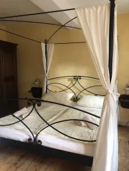 Ein gemütliches Schlafzimmer mit einem schwarzen Himmelbett und weißen Vorhängen. Die Wände sind in sanften Gelbtönen gestrichen, und es gibt einen Holzschrank im Raum.