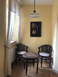 Eine gemütliche Ecke mit zwei Holzstühlen und einem kleinen Tisch. An der Wand hängt ein Bild und die Wände sind in sanften Gelbtönen gestrichen.