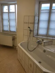 Ein modernes Badezimmer mit einer großen Badewanne und einem Fenster. Der Raum ist hell und gut ausgestattet.