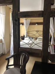 Ein gemütliches Schlafzimmer mit rustikalen Holzbalken und einem Bett mit einem Metallrahmen. Die warmen Farben und das natürliche Licht schaffen eine einladende Atmosphäre.