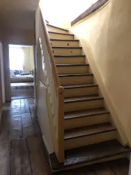 Eine helle Treppe mit Holzstufen führt zu einem oberen Stockwerk. Im Hintergrund ist einWohnraum mit weichen Möbeln zu sehen.