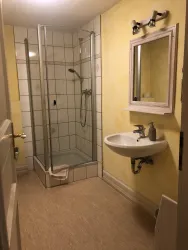 Ein einfaches Badezimmer mit einer Duschkabine und einem Waschbecken. Die Wände sind gelb gestrichen und die Fliesen sind hell.