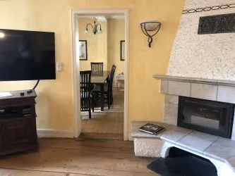 Ein gemütliches Wohnzimmer mit einem Fernseher und einem Kamin. Im Hintergrund ist ein Essbereich mit einem Tisch und Stühlen zu sehen.