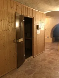 Ein Holzsauna-Eingang in einem warmen, einladenden Raum. Der Boden ist mit Fliesen ausgestattet und die Wände sind mit Holzverkleidungen gestaltet.