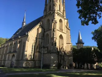 Eine beeindruckende Kirche mit hohen Türmen und detaillierter Architektur. Der klare Himmel und die üppigen Bäume umgeben das Gebäude.