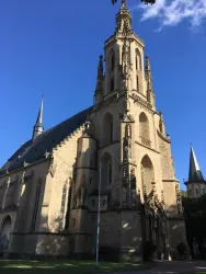 Eine beeindruckende Kirche mit hohen Türmen und einer kunstvollen Fassade. Der blaue Himmel und die Sonnenstrahlen verleihen der Szenerie zusätzlichen Charme.