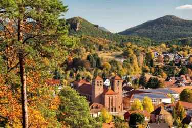 Eine malerische Stadt mit historischen Gebäuden und bunten herbstlichen Bäumen. Im Hintergrund erheben sich sanfte Hügel und Berge.