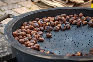 Geröstete Kastanien in einer großen, schwarzen Pfanne. Die Kastanien sind braun und glänzend, bereit zum Verzehr.