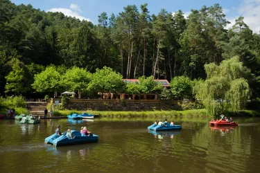 Eine malerische Landschaft mit einem ruhigen See und Booten, die darauf fahren. Im Hintergrund sind üppige Bäume und ein gemütliches Gebäude zu sehen.