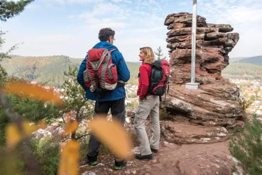 Zwei Wanderer stehen auf einem Aussichtspunkt mit Blick auf die Landschaft. Die Umgebung ist bewaldet und die Felsen sind sichtbar.