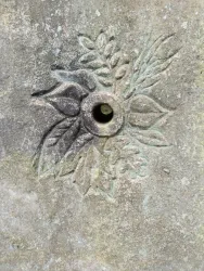 Eine dekorative Steinoberfläche mit einem eingravierten Pflanzenmotiv. In der Mitte befindet sich ein Loch.