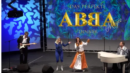 Eine musikalische Aufführung mit vier Darstellern auf einer Bühne. Im Hintergrund ist ein großes, farbenfrohes Banner mit dem Schriftzug "ABBA Magic".