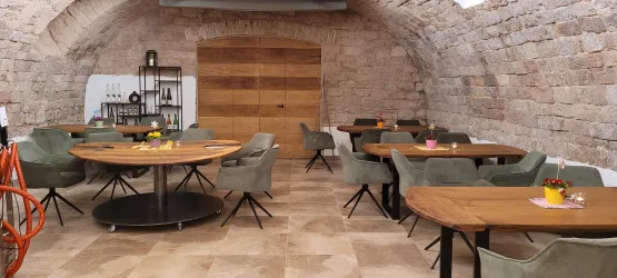 Ein gemütliches Restaurant mit runden Holztischen und modernen Stühlen. Die steinernen Wände verleihen dem Raum eine warme Atmosphäre.
