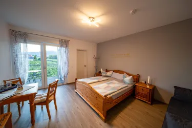 Ein gemütliches Schlafzimmer mit Holzmöbeln und einem großen Fenster, das einen Blick auf die Natur bietet. Ein Tisch und Stühle ergänzen den Raum für entspannte Momente.