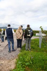 Eine Gruppe von Menschen steht auf einem Weg in einer Weinregion und schaut in die Ferne. Ein Schild mit der Beschriftung "Weingut Anselmann" ist sichtbar.
