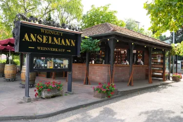 Ein Weingut mit einem einladenden Verkaufshäuschen und einer schönen Terrasse. Blumen und Weinfässer dekorieren den Außenbereich.