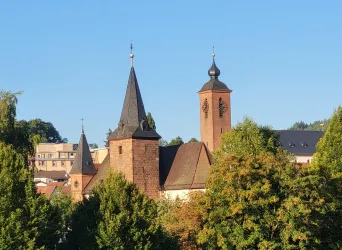 Eine historische Kirche mit zwei Türmen und grünem Baumbewuchs. Der Himmel ist klar und blau.