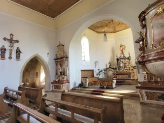 Eine elegante Kirche mit Holzbankreihen und einer reich verzierten altarischen Einrichtung. Die Wände sind geschmückt mit religiösen Figuren und Kreuzen.