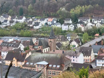 Eine malerische Stadt mit vielen bunten Häusern und einem markanten Kirchturm. Die Umgebung ist grün und hügelig, was der Szene eine charmante Atmosphäre verleiht.