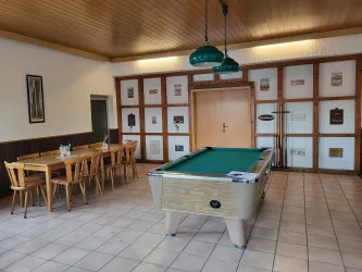 Ein gemütlicher Raum mit einem Billardtisch und einer Essbereich. Wände mit Bildern und Holzverkleidung sorgen für eine einladende Atmosphäre.