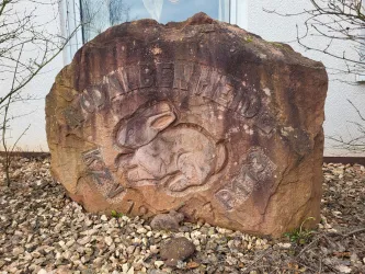 Ein großer, bemalter Stein mit einer Darstellung eines Kaninchens. Der Stein hat eingravierte Buchstaben und liegt zwischen kleinen Steinen.