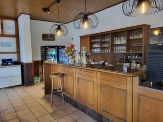 Eine gemütliche Bar mit holzverkleidetem Thekenbereich und dekorativen Lampen. Auf der Theke stehen Getränke und eine Blumenarrangement.