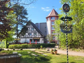 Ein einladendes Gebäude im ländlichen Stil, umgeben von Bäumen und grünem Gras. Ein Schild mit der Aufschrift "Biergarten" steht im Vordergrund.