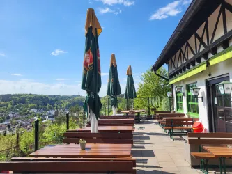 Eine Terrasse mit Holztischen und Sonnenschirmen bietet einen schönen Blick auf die Landschaft. Der Himmel ist klar und die Umgebung ist grün.