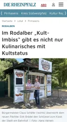 Ein Imbissstand mit dem Namen "Rodalber Kult-Imbiss" steht in einem grünen Bereich. Bürgermeister Claus Schäfer übergibt den Schlüssel an den neuen Pächter Dirk Brödel.