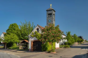 Ein charmantes Gebäude mit einem hohen Turm und einer Uhr. Umgeben von grünen Bäumen und einem klaren blauen Himmel.