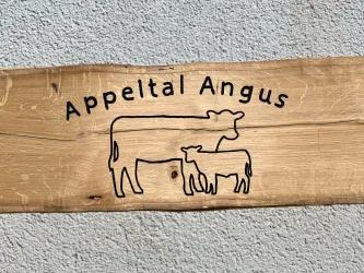 Ein Holzschild mit der Aufschrift "Appeltal Angus". Darauf sind eine Kuh und ein Kalb in konturiertem Stil abgebildet.