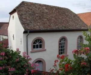 Ein schönes, traditionelles Gebäude mit einem gedämmten Dach. Es ist von Blumen umgeben und hat große Fenster im klassisch-ästhetischen Stil.