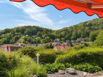 Eine malerische Landschaft mit sanften Hügeln und üppigem Grün. Im Vordergrund sind Pflanzen und Sträucher sichtbar, während die hellen Häuser in der Ferne sichtbar sind.
