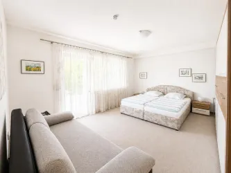 Ein helles Schlafzimmer mit einem Doppelbett und einem Sofa. Große Fenster lassen viel Tageslicht herein.