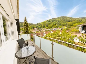 Ein schöner Balkon mit Blick auf grüne Hügel und ein malerisches Dorf. Ein Tisch mit zwei Stühlen lädt zum Entspannen ein.