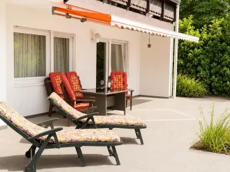 Eine gemütliche Terrasse mit Liegen und einem Tisch. Umgeben von grünen Pflanzen und einem einladenden Ambiente.