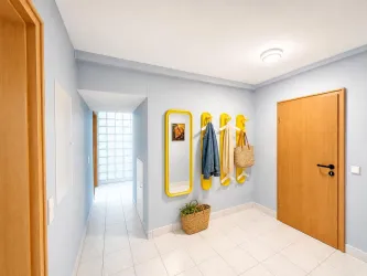 Ein heller Flur mit blauen Wänden und weißen Fliesen. An der Wand hängen gelbe Kleiderhaken mit einer Jacke und einer Tasche.