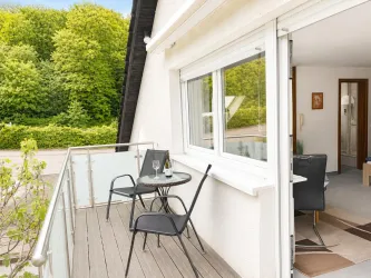 Ein gemütlicher Balkon mit zwei Stühlen und einem kleinen Tisch. Im Hintergrund sind grüne Bäume zu sehen.