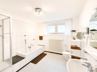 Ein modernes Badezimmer mit Dusche und Badewanne. Helle Fliesen und große Fenster sorgen für eine freundliche Atmosphäre.