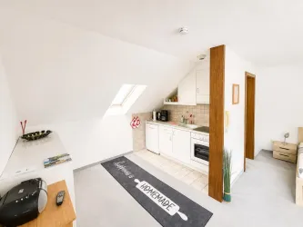 Eine moderne Dachgeschosswohnung mit offener Küche und gemütlichem Wohnbereich. Helle Farben und ein einfacher Stil schaffen eine einladende Atmosphäre.