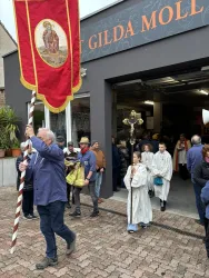 Eine Prozession mit Menschen, die eine Fahne tragen. Im Hintergrund ist ein Gebäude mit dem Schriftzug "Gilda Moll" zu sehen.