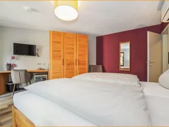 Ein modernes Schlafzimmer mit zwei Betten und hellen Farben. Der Raum verfügt über einen Schreibtisch, einen Fernseher und einen Spiegel.