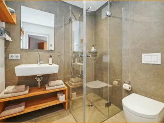 Ein modernes Badezimmer mit einer gläsernen Dusche und einem Waschbecken auf einem Holzregal. Die Wände sind mit fliesen in warmen Farbtönen gestaltet.